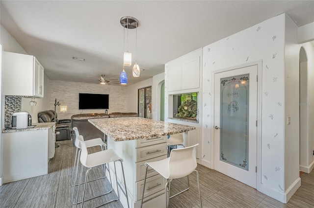 kitchen featuring white cabinetry, a kitchen bar, hanging light fixtures, a center island, and light stone counters