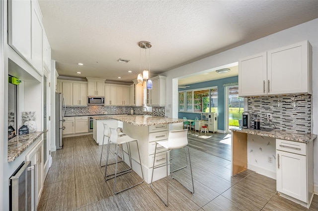 kitchen featuring hanging light fixtures, a breakfast bar area, light stone countertops, and appliances with stainless steel finishes