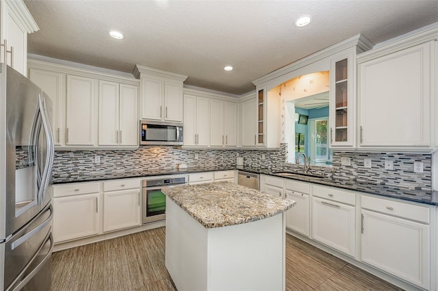 kitchen with sink, appliances with stainless steel finishes, a center island, tasteful backsplash, and dark stone counters