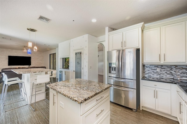 kitchen featuring decorative light fixtures, a kitchen island, dark stone counters, and stainless steel refrigerator with ice dispenser