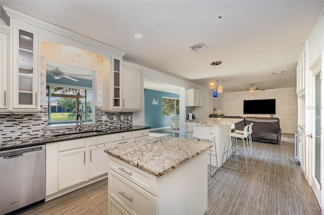 kitchen featuring pendant lighting, sink, dishwasher, white cabinetry, and a center island