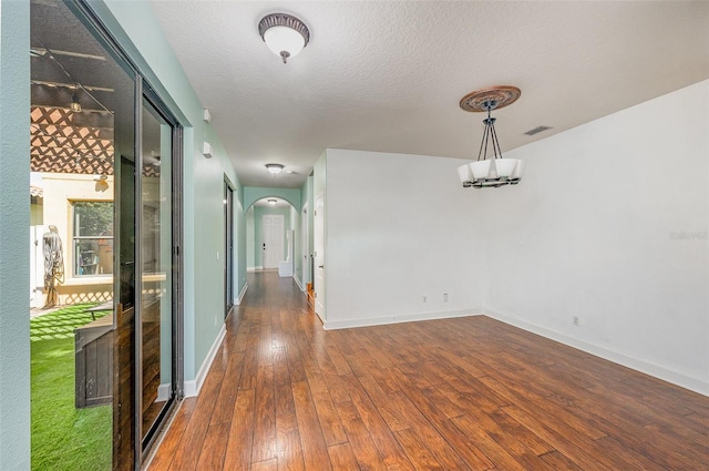 unfurnished room featuring an inviting chandelier, dark hardwood / wood-style flooring, and a textured ceiling