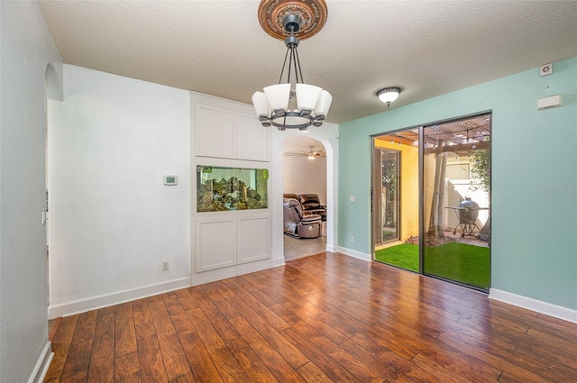 spare room featuring dark hardwood / wood-style flooring, ceiling fan with notable chandelier, and a textured ceiling