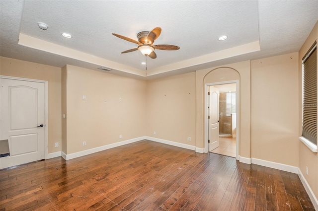 unfurnished room featuring ceiling fan, wood-type flooring, a raised ceiling, and a textured ceiling