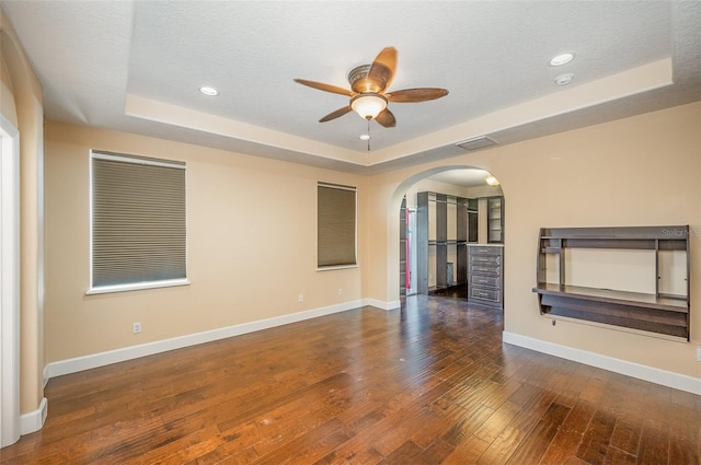 spare room with ceiling fan, dark hardwood / wood-style floors, a raised ceiling, and a textured ceiling