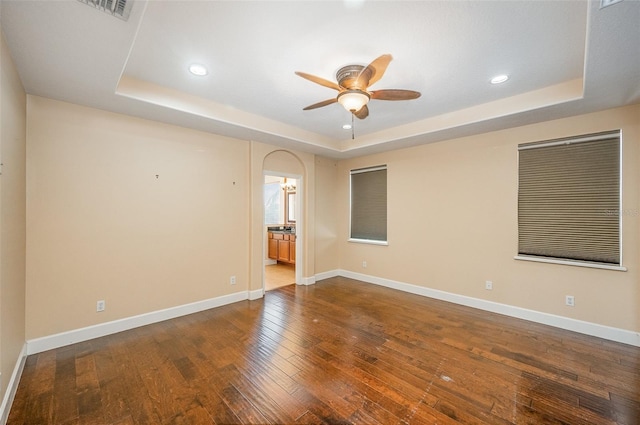 empty room with hardwood / wood-style flooring, ceiling fan, and a tray ceiling