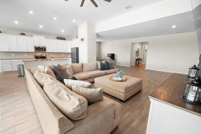 living room with ceiling fan, vaulted ceiling, and light hardwood / wood-style flooring