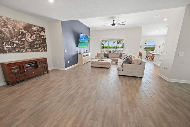 living room with ceiling fan, a textured ceiling, and light wood-type flooring