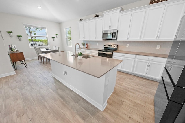 kitchen featuring sink, stainless steel appliances, a kitchen island with sink, decorative backsplash, and white cabinets