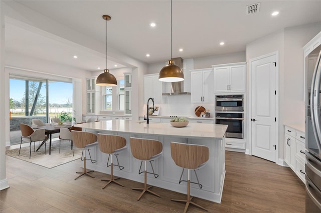 kitchen with hardwood / wood-style floors, double oven, white cabinetry, hanging light fixtures, and a kitchen island with sink