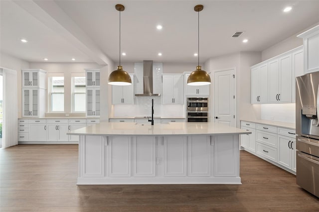 kitchen featuring pendant lighting, a kitchen island with sink, wall chimney exhaust hood, and appliances with stainless steel finishes