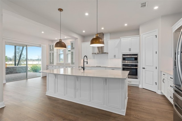 kitchen with decorative light fixtures, white cabinetry, decorative backsplash, stainless steel double oven, and a center island with sink