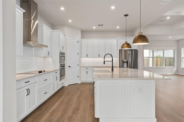 kitchen featuring sink, appliances with stainless steel finishes, wall chimney range hood, a kitchen island with sink, and white cabinets