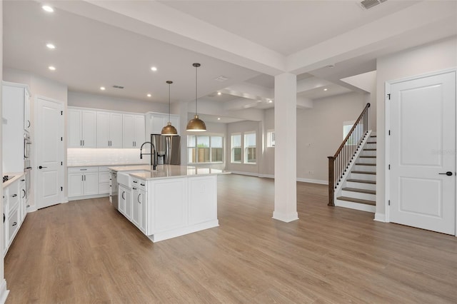 kitchen with white cabinetry, decorative light fixtures, stainless steel appliances, a kitchen island with sink, and backsplash