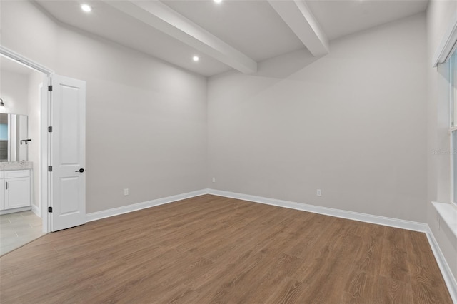 spare room with beamed ceiling and light hardwood / wood-style flooring