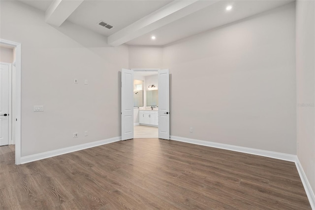 unfurnished bedroom featuring beamed ceiling, dark hardwood / wood-style floors, and ensuite bath