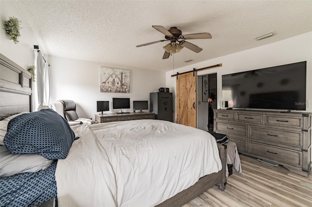 bedroom with a textured ceiling, light hardwood / wood-style flooring, a barn door, and ceiling fan