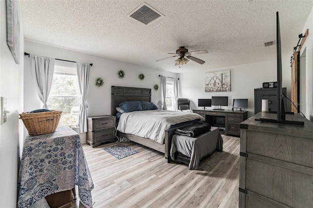 bedroom with ceiling fan, a barn door, a textured ceiling, and light wood-type flooring