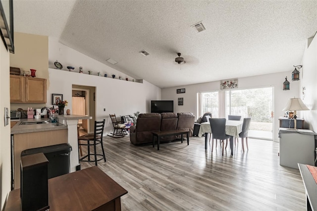 living room with vaulted ceiling, sink, light wood-type flooring, ceiling fan, and a textured ceiling