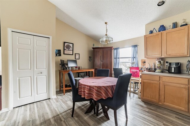 dining room with lofted ceiling, light hardwood / wood-style floors, and a textured ceiling