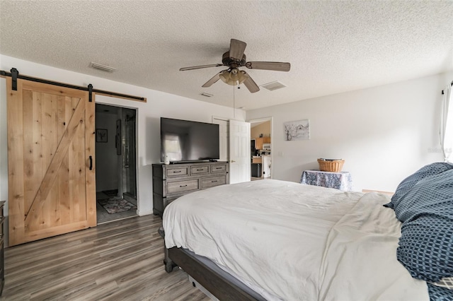 bedroom featuring dark wood-type flooring, connected bathroom, a textured ceiling, ceiling fan, and a barn door