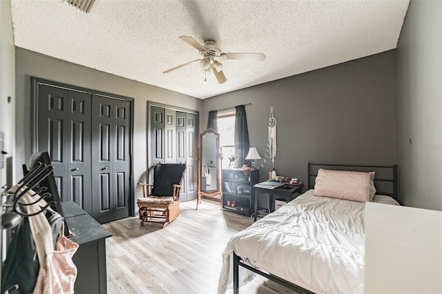 bedroom with multiple closets, a textured ceiling, ceiling fan, and light hardwood / wood-style floors