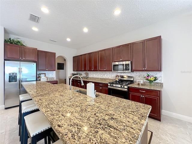 kitchen with a kitchen bar, sink, tasteful backsplash, stainless steel appliances, and a kitchen island with sink