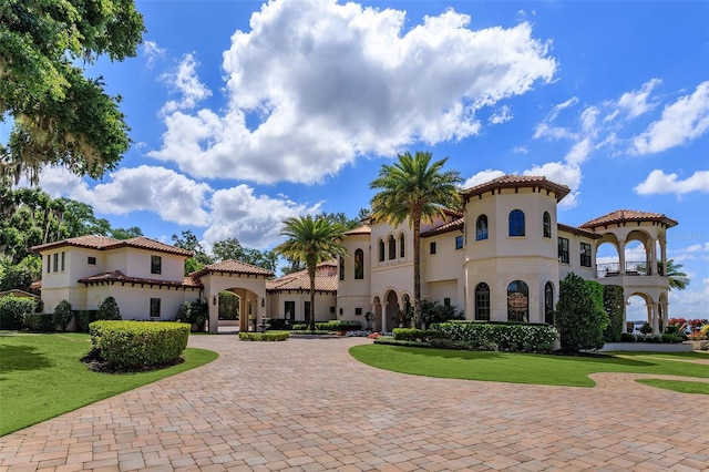 mediterranean / spanish-style home featuring a front lawn, a tiled roof, curved driveway, and stucco siding