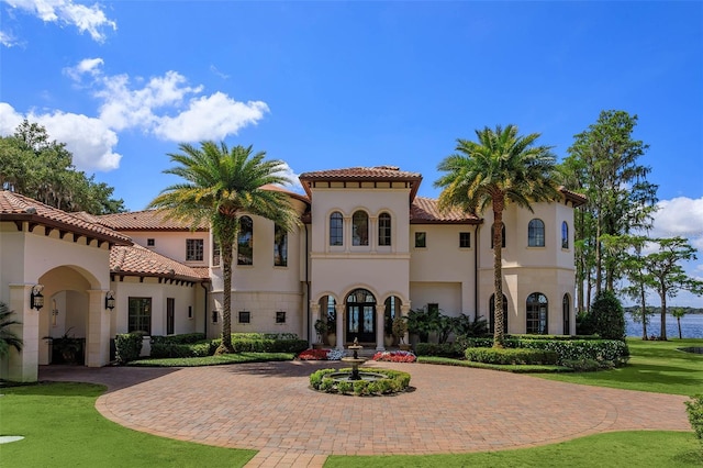 view of front of house featuring stucco siding, a tiled roof, a front lawn, and curved driveway