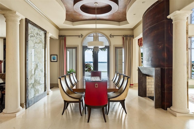 dining space with ornamental molding, a raised ceiling, and decorative columns