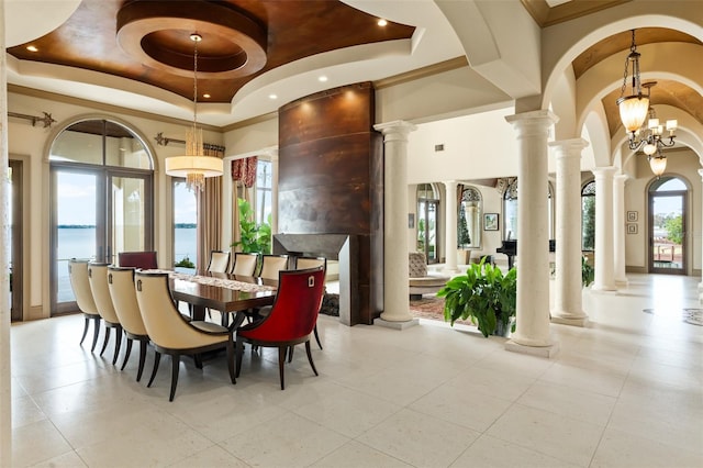 dining space featuring a water view, ornamental molding, a high ceiling, a raised ceiling, and ornate columns