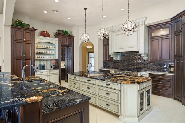 kitchen featuring visible vents, a sink, tasteful backsplash, arched walkways, and a large island with sink