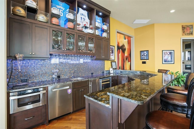 kitchen with a kitchen bar, backsplash, wine cooler, appliances with stainless steel finishes, and a peninsula