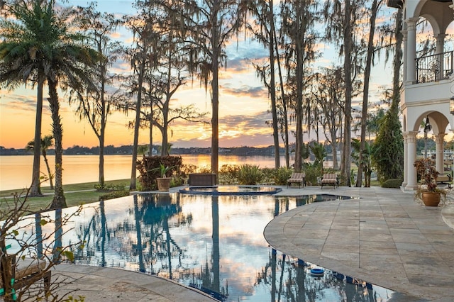 pool at dusk with a jacuzzi, a water view, and a patio area