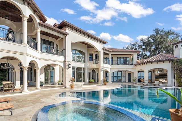 rear view of house featuring a pool with connected hot tub, stucco siding, french doors, a balcony, and a patio area