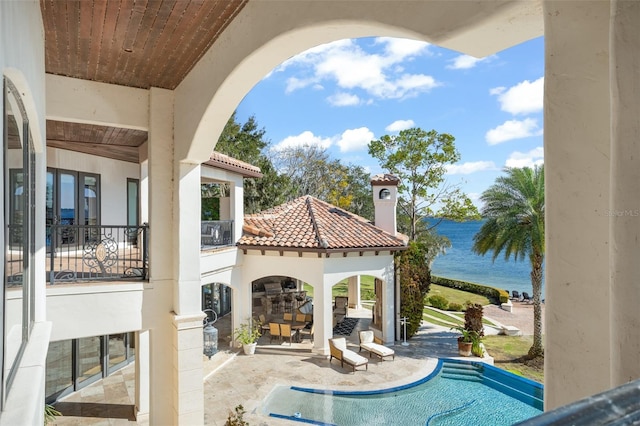 view of patio with a balcony, an outdoor pool, and a water view