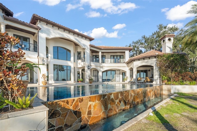 back of property featuring stucco siding, a patio, a balcony, and an infinity pool