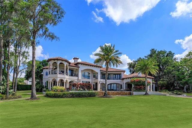 back of property featuring a yard, a balcony, a tile roof, and stucco siding