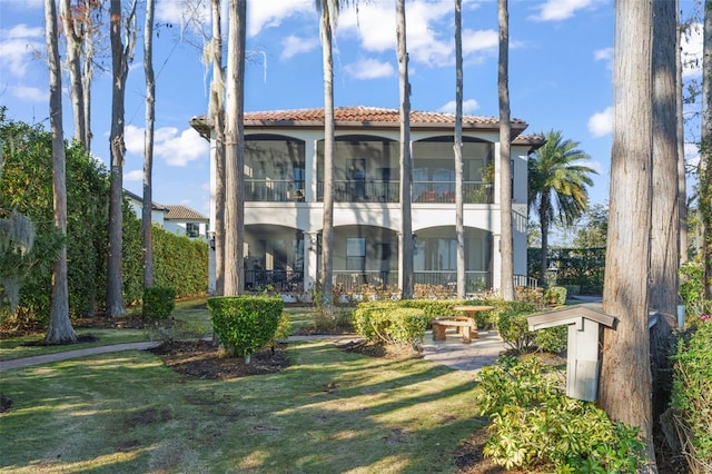 rear view of property with a tile roof, a yard, and stucco siding