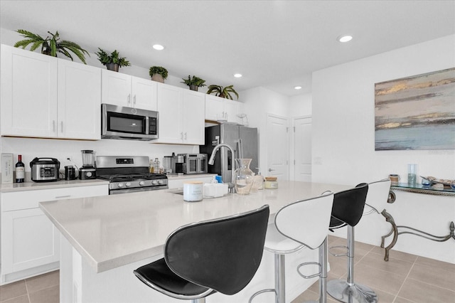 kitchen featuring white cabinetry, light tile patterned floors, a kitchen breakfast bar, an island with sink, and stainless steel appliances