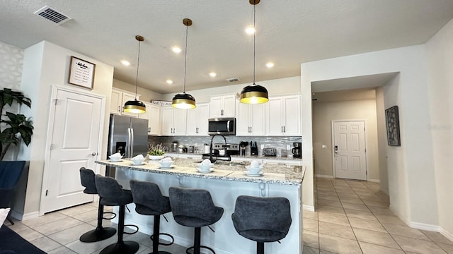 kitchen with stainless steel appliances, an island with sink, hanging light fixtures, and light tile patterned floors