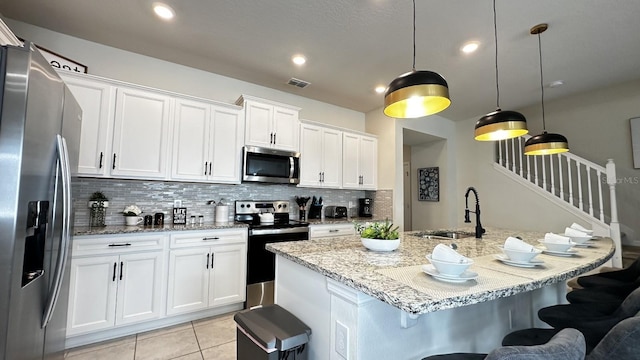 kitchen with sink, hanging light fixtures, appliances with stainless steel finishes, a kitchen island with sink, and white cabinets