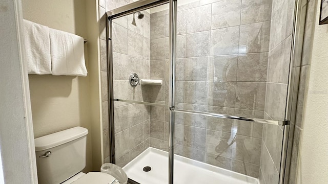 bathroom featuring a shower with door and toilet