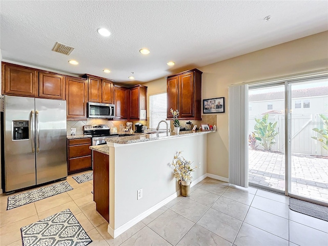 kitchen featuring light stone countertops, appliances with stainless steel finishes, a healthy amount of sunlight, and kitchen peninsula