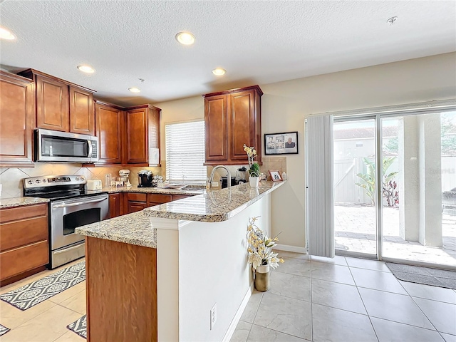 kitchen with stainless steel appliances, light stone countertops, light tile patterned floors, and kitchen peninsula