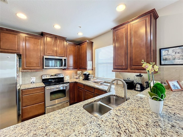 kitchen featuring sink, decorative backsplash, light stone countertops, and appliances with stainless steel finishes