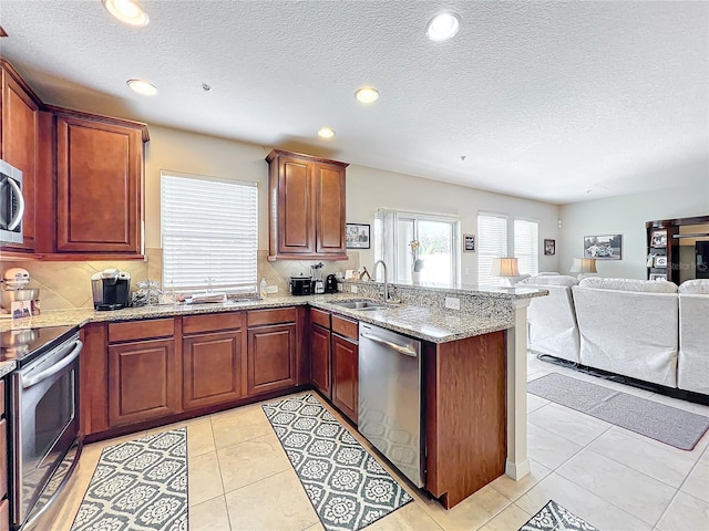 kitchen featuring stainless steel appliances, kitchen peninsula, sink, and light stone countertops