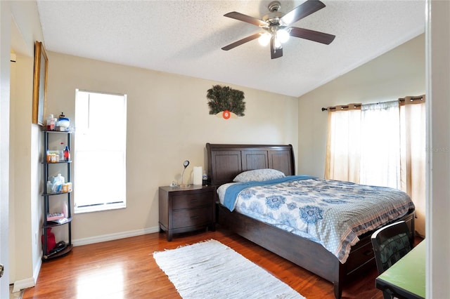 bedroom featuring baseboards, ceiling fan, wood finished floors, vaulted ceiling, and a textured ceiling