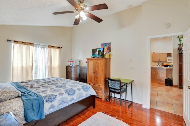 bedroom with a ceiling fan, vaulted ceiling, a textured ceiling, wood finished floors, and baseboards