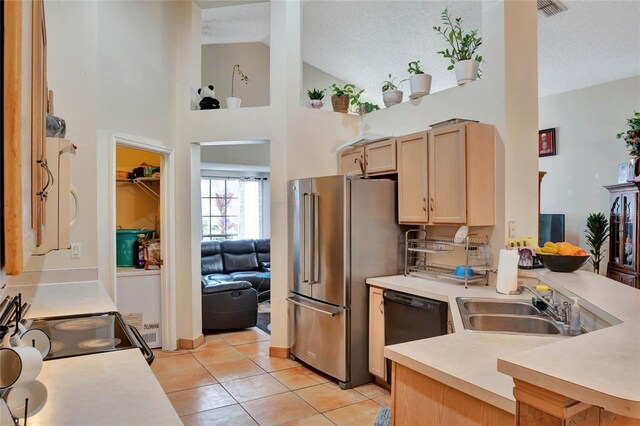 kitchen with black dishwasher, freestanding refrigerator, light countertops, light brown cabinetry, and a sink